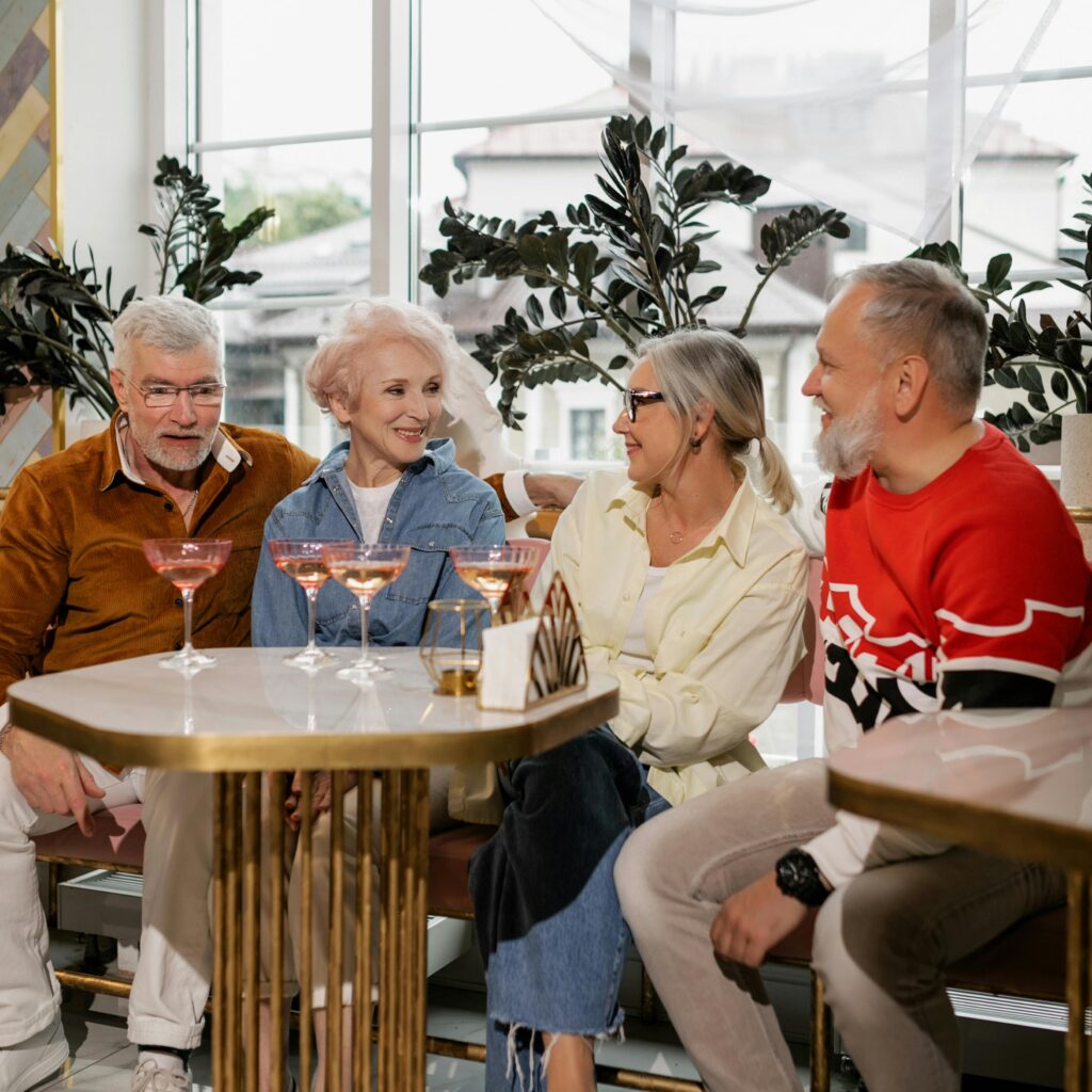 Four senior adults sharing a joyful moment with drinks in a cozy indoor cafe setting.