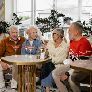 Four senior adults sharing a joyful moment with drinks in a cozy indoor cafe setting.