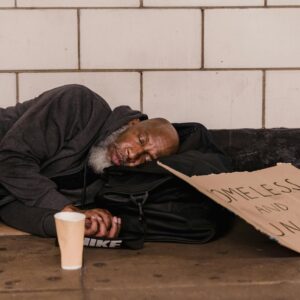 African American man sleeping in subway with sign, highlighting social issues.